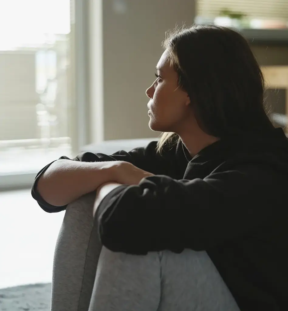 Eine junge Frau sitzt auf dem Boden und blickt nachdenklich in die Weite.