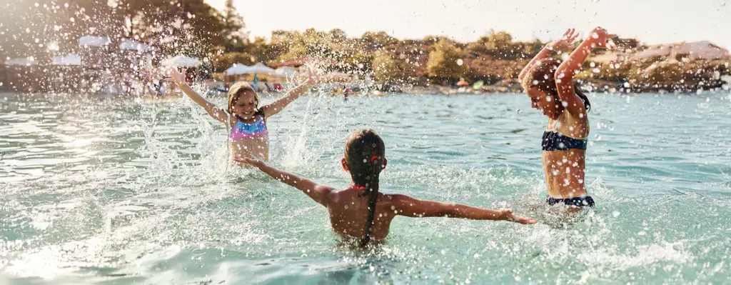 Drei Kinder spielen und spritzen lachend im flachen Wasser am Strand