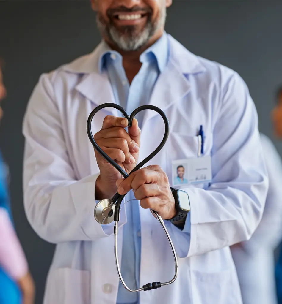 Arzt im weißen Kittel hält ein Stethoskop in Herzform vor sich