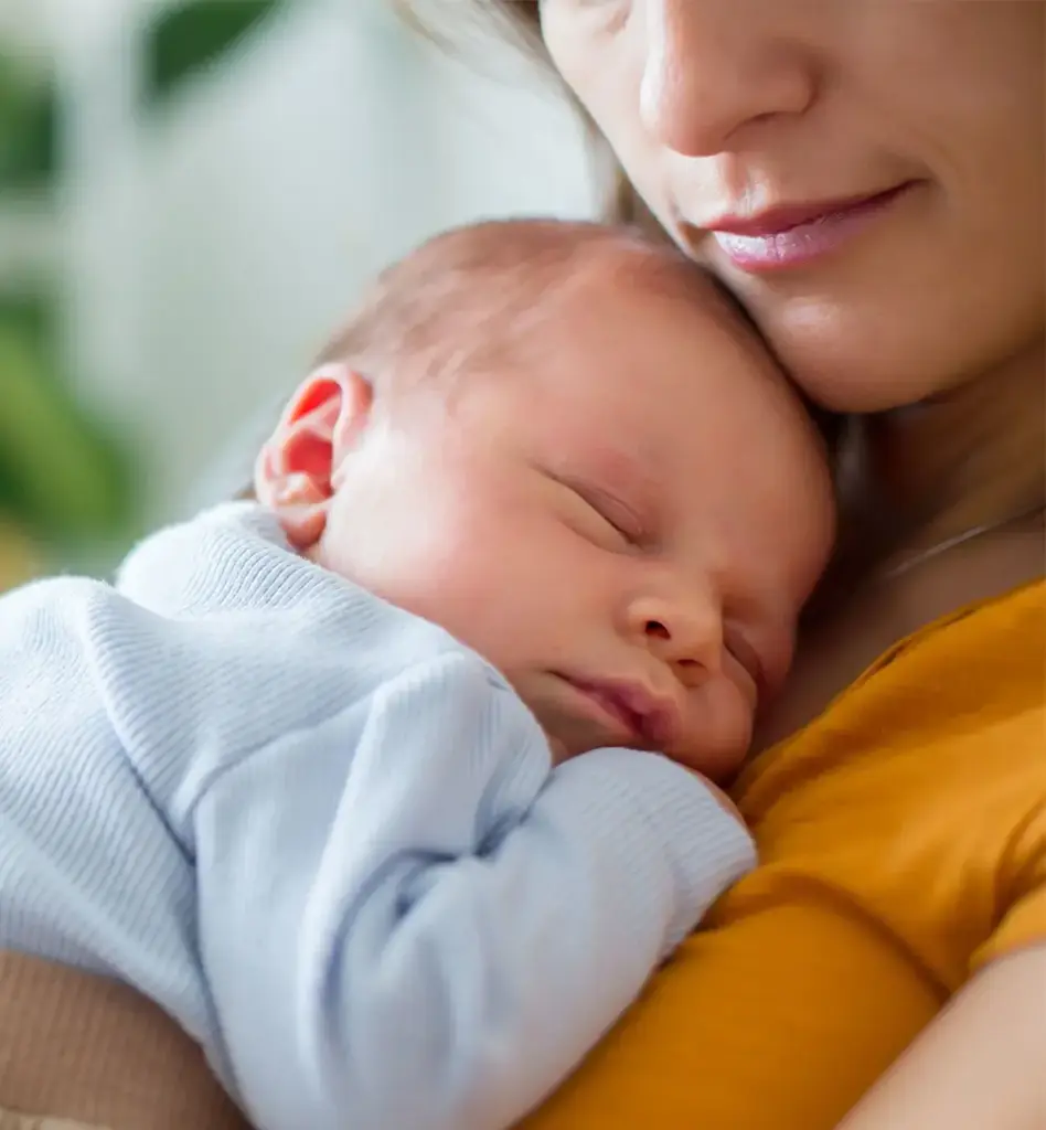 Schlafendes Neugeborenes in hellblauem Strampler liegt friedlich auf der Brust der Mutter – zartes, emotionales Close-up.