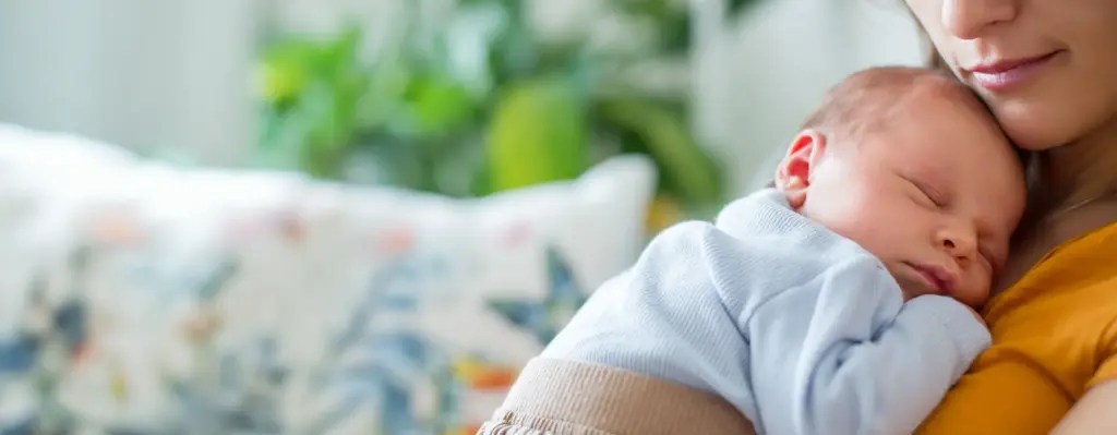 Schlafendes Neugeborenes in hellblauem Strampler liegt friedlich auf der Brust der Mutter – zartes, emotionales Close-up.