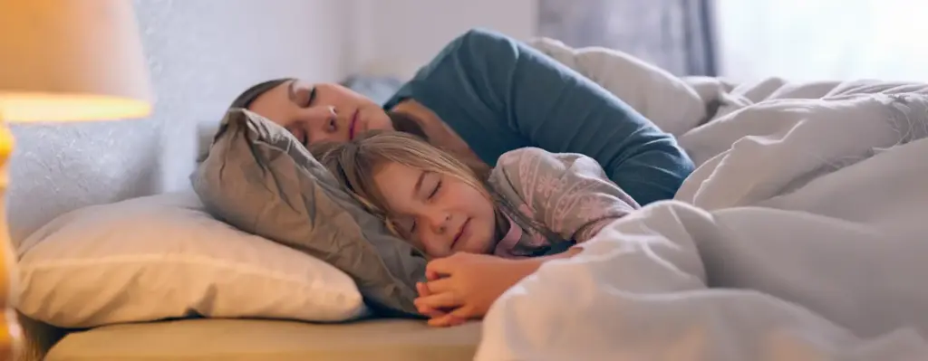 Mutter und Tochter schlafen friedlich nebeneinander im Bett – warme, geborgene Atmosphäre.