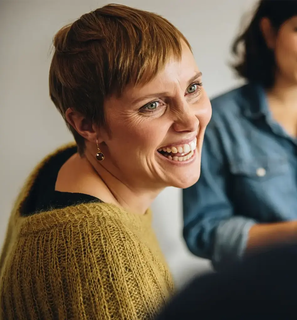 Frau mit kurzem Haar lacht herzlich und schaut eine andere Person an – nahaufnahme, warme und lebendige Atmosphäre.