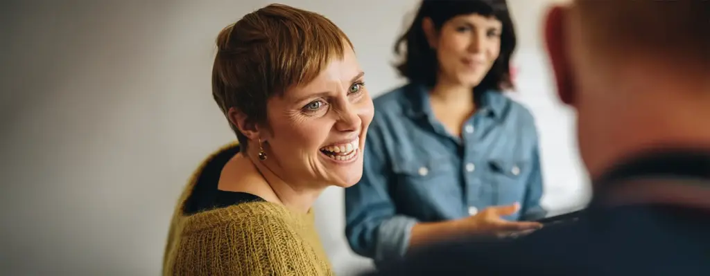Frau mit kurzem Haar lacht herzlich und schaut eine andere Person an – nahaufnahme, warme und lebendige Atmosphäre.