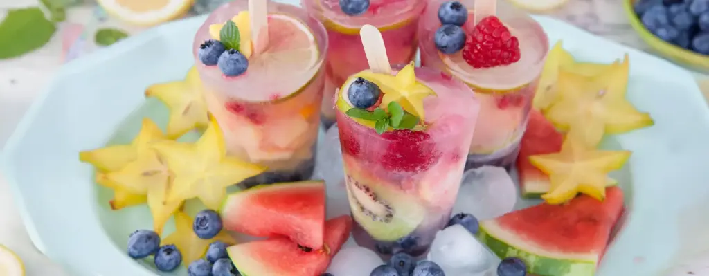 Selbstgemachte bunte Wassereis-Becher mit Beeren, Kiwi und Wassermelonenstücken auf Eiswürfeln – gesundes Sommer-Eis zum Selbermachen.