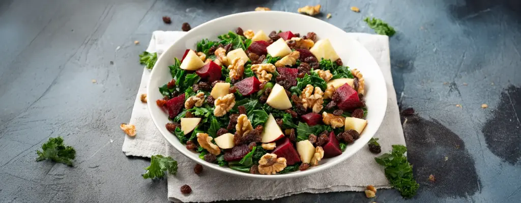 Wintersalat mit Grünkohl, Roten Beten, Apfelstücken, Walnüssen und Rosinen in einer weißen Schüssel – gesunde Winterküche.
