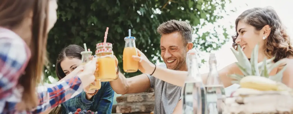 Gruppe junger Leute stößt draußen am Tisch fröhlich mit Saftschorlen in Gläsern an – geselliges Beisammensein im Freien.