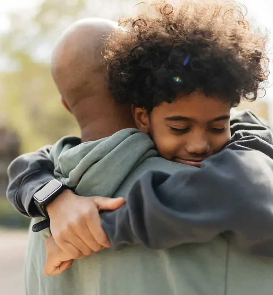 Vater umarmt seinen Sohn herzlich – Kind schmiegte sich lächelnd an den Vater, innige Vater-Kind-Szene im Freien.