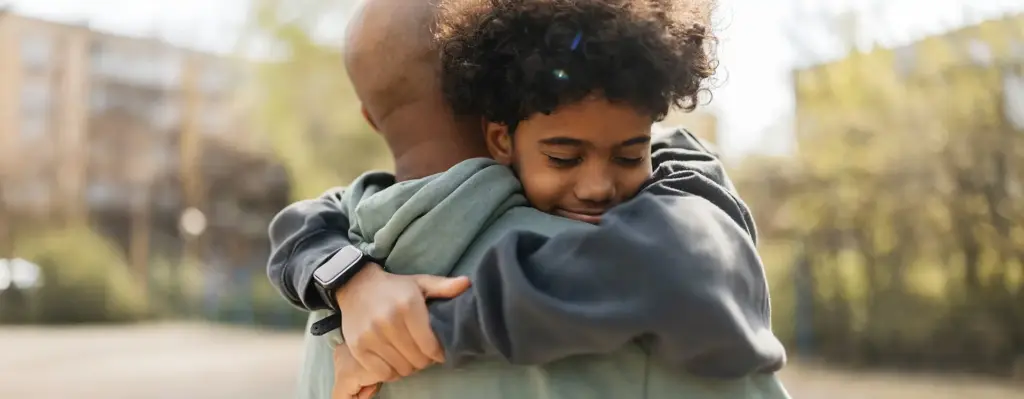 Vater umarmt seinen Sohn herzlich – Kind schmiegte sich lächelnd an den Vater, innige Vater-Kind-Szene im Freien.