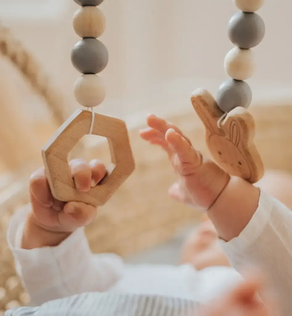 Nahaufnahme: Baby greift mit beiden Händchen nach hängenden Holzspielzeugen eines Babylernspiels – neugierige Erkundung.