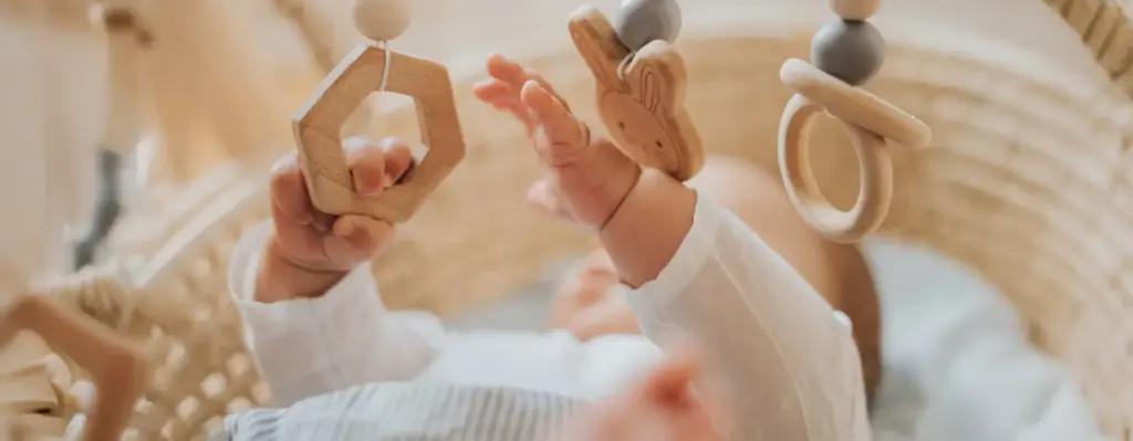Nahaufnahme: Baby greift mit beiden Händchen nach hängenden Holzspielzeugen eines Babylernspiels – neugierige Erkundung.