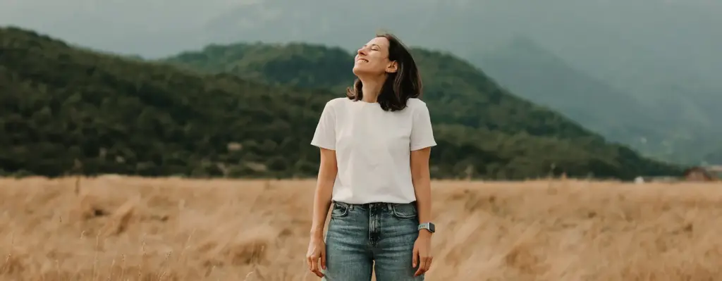 Eine Frau steht auf einem Feld und blickt mit geschlossenen Augen und gehobenen Kopf Richtung Himmel. Das Bild wird im Bereich "Arzneimittel Homöopathie, Phytotherapie und Anthroposophie" verwendet.