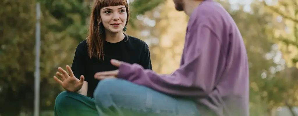Eine junge Frau und ein junger Mann sitzen im Schneidersitz auf einer Wiese und unterhalten sich. Das Bild wird im Bereich "AzubiPlus Wahltarif - ist bares Geld wert!" verwendet.