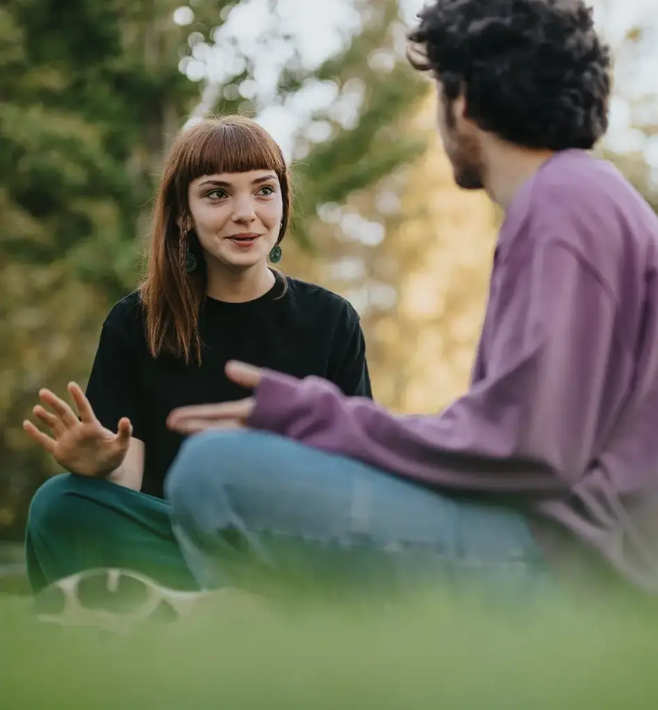 Eine junge Frau und ein junger Mann sitzen im Schneidersitz auf einer Wiese und unterhalten sich. Das Bild wird im Bereich "AzubiPlus Wahltarif - ist bares Geld wert!" verwendet.