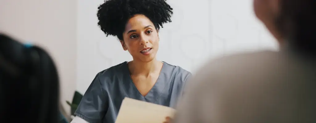 Eine Frau hält ein Dokument in der Hand und blickt auf einen Mann, der vor ihr sitzt. Das Bild wird im Bereich "Individuelle Gesundheitsleistungen (IGeL)" verwendet.