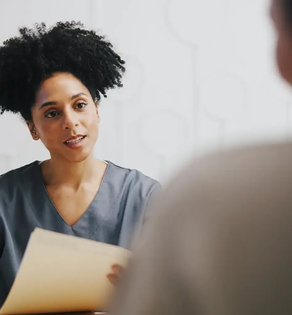 Eine Frau hält ein Dokument in der Hand und blickt auf einen Mann, der vor ihr sitzt. Das Bild wird im Bereich "Individuelle Gesundheitsleistungen (IGeL)" verwendet.