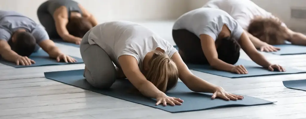 Eine Gruppe von Frauen macht die Pose des Kindes, auch Balasana genannt. Sie knien dabei auf Fitnessmatten. Das Bild wird im Bereich "Ambulante Vorsorgekuren" verwendet.