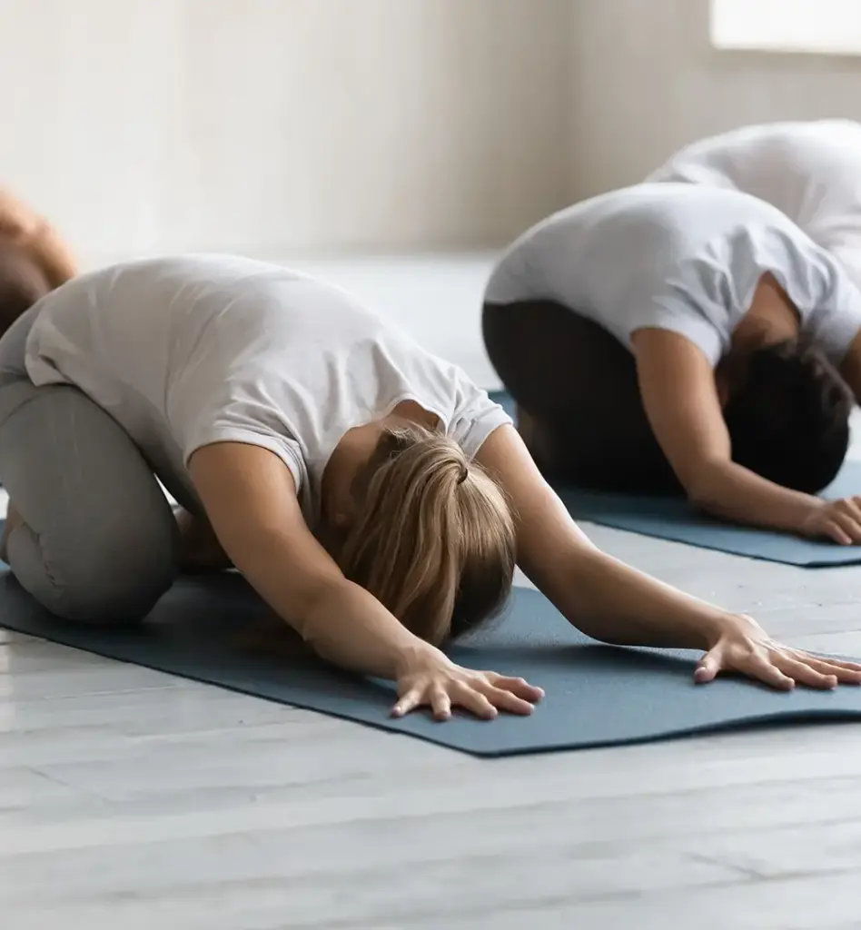 Eine Gruppe von Frauen macht die Pose des Kindes, auch Balasana genannt. Sie knien dabei auf Fitnessmatten. Das Bild wird im Bereich "Ambulante Vorsorgekuren" verwendet.