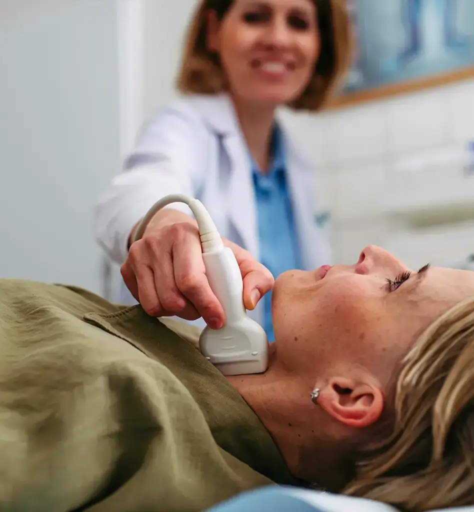 Eine Ärztin misst eine Arterie am Hals einer Frau, die auf einer Behandlungsliege liegt. Das Bild wird im Bereich "Arteriencheck (Intima-Media-Dicke-Messung)" verwendet.