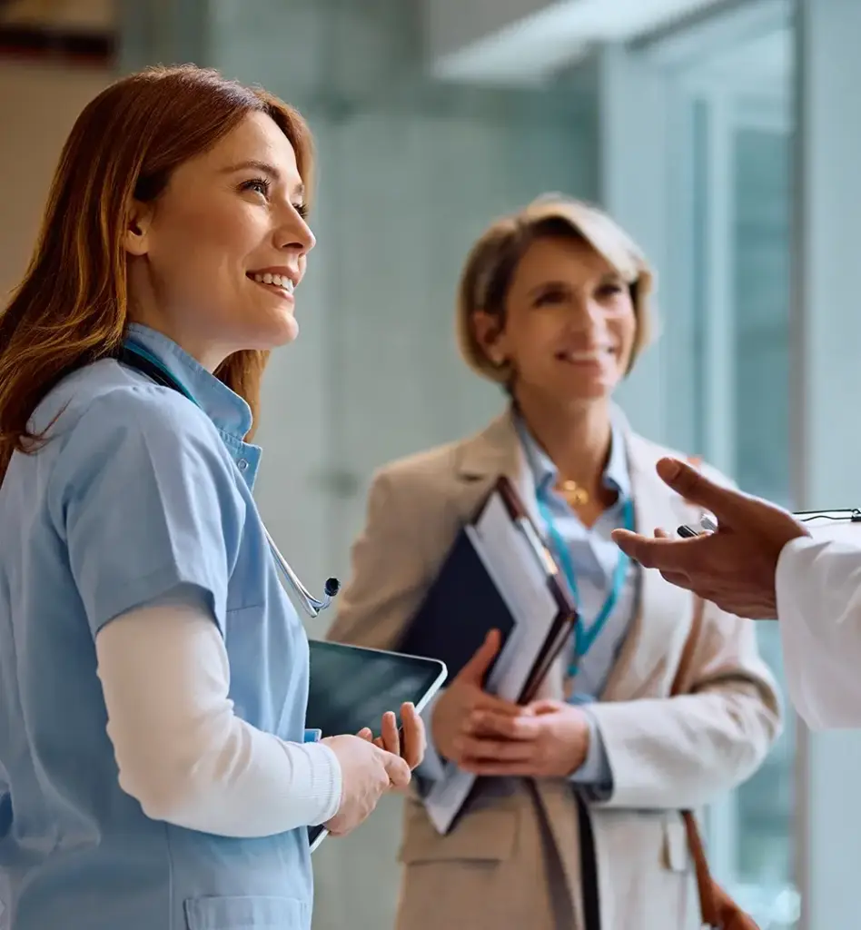 Zwei Frauen, die vermutlich im Krankenhaus arbeiten, sprechen mit einem nur am Bildrand zu erahnenden Arzt. Das Bild wird im Bereich "Arztfinder" verwendet.