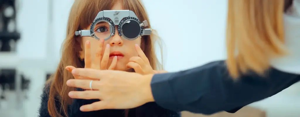 Ein Mädchen sitzt an einem Instrument bei einem Augenarzt. Das Bild wird im Bereich "Augenscreening für Kinder" verwendet.