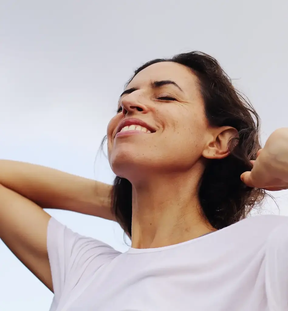 Eine Frau hat ihren Kopf Richtung Himmel gehoben und die Augengeschlossen. Ihre Hände hat sie ebenfalls an den Kopf gehoben. Das Bild wird im Bereich "Brustkrebsvorsorge – discovering hands" verwendet.