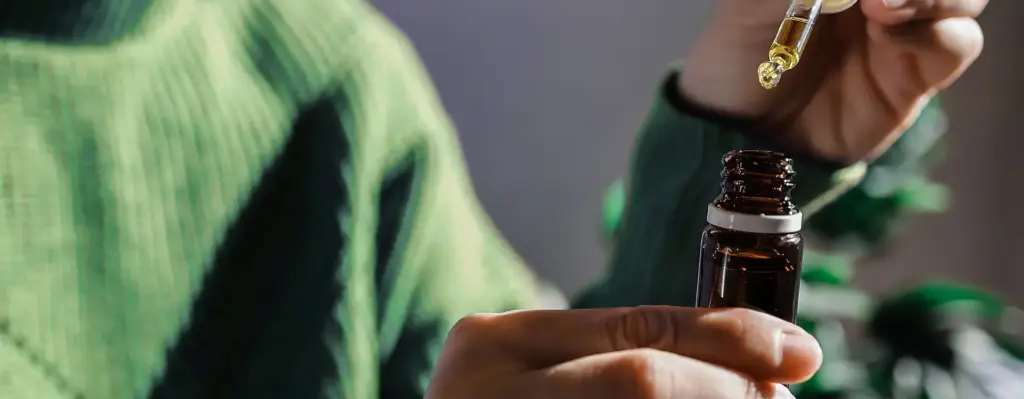 Das Bild zeigt eine Nahaufnahme zweier Hände, die ein Glasfläschchen und eine Pipette halten. Das Bild wird im Bereich "Cannabis Behandlung" verwendet.