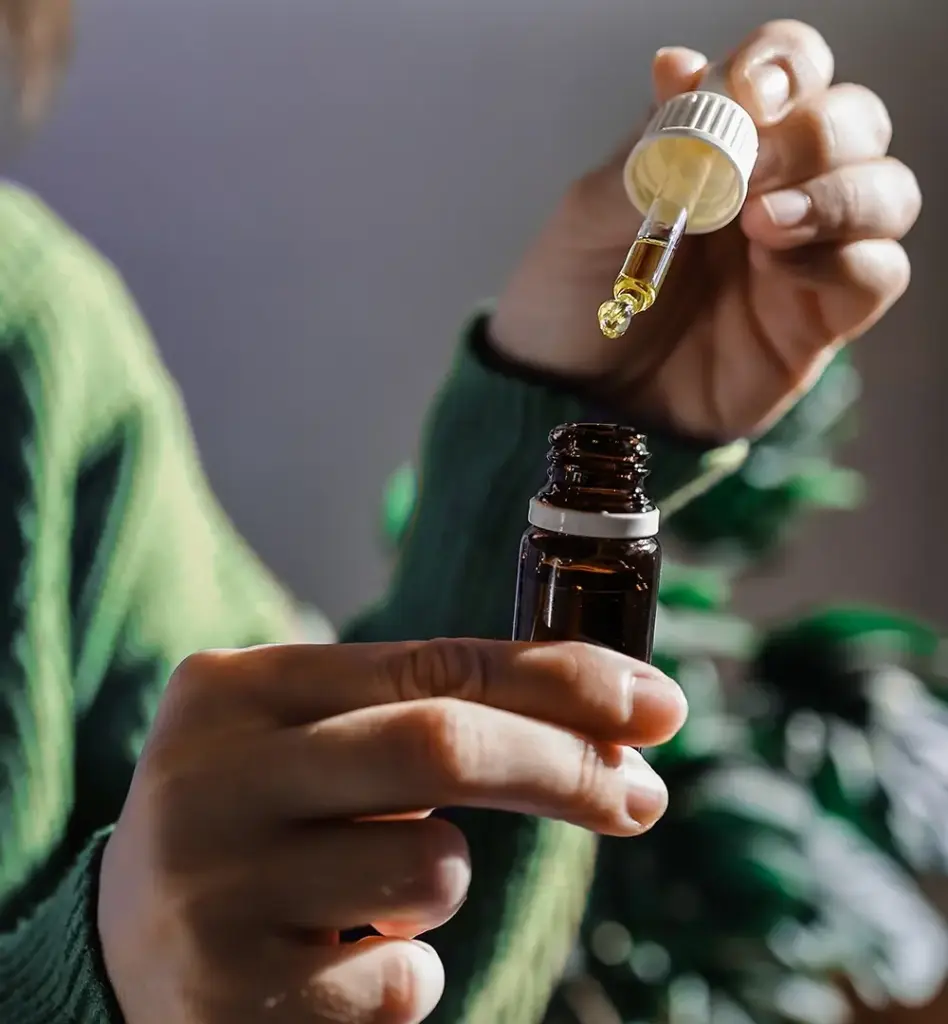 Das Bild zeigt eine Nahaufnahme zweier Hände, die ein Glasfläschchen und eine Pipette halten. Das Bild wird im Bereich "Cannabis Behandlung" verwendet.