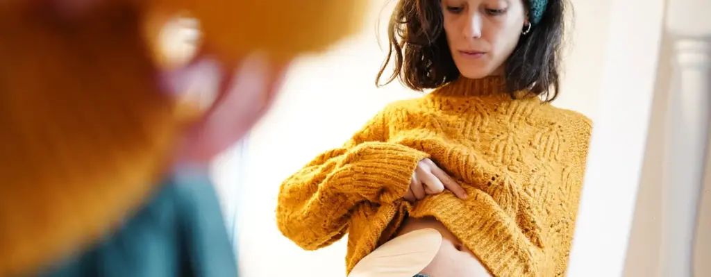 Eine Frau steht vor einem Spiegel und blickt an sich herunter. Sie hat einen künstlichen Darmausgang. Das Bild wird im Bereich "Darmkrebs Früherkennung" verwendet.