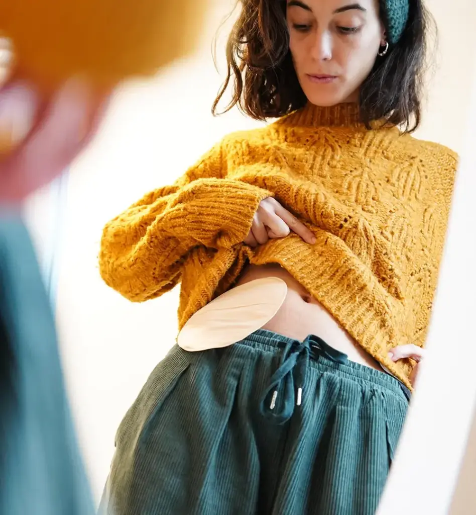 Eine Frau steht vor einem Spiegel und blickt an sich herunter. Sie hat einen künstlichen Darmausgang. Das Bild wird im Bereich "Darmkrebs Früherkennung" verwendet.