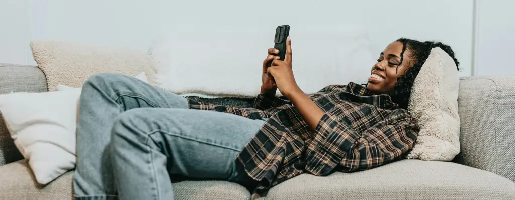 Eine Frau liegt auf der Couch und schaut auf ihr Smartphone. Das Bild wird im Bereich "Disease-Management-Programm (DMP) für chronisch Erkrankte" verwendet.