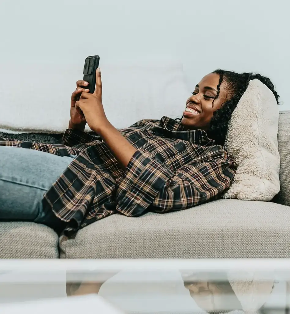 Eine Frau liegt auf der Couch und schaut auf ihr Smartphone. Das Bild wird im Bereich "Disease-Management-Programm (DMP) für chronisch Erkrankte" verwendet.