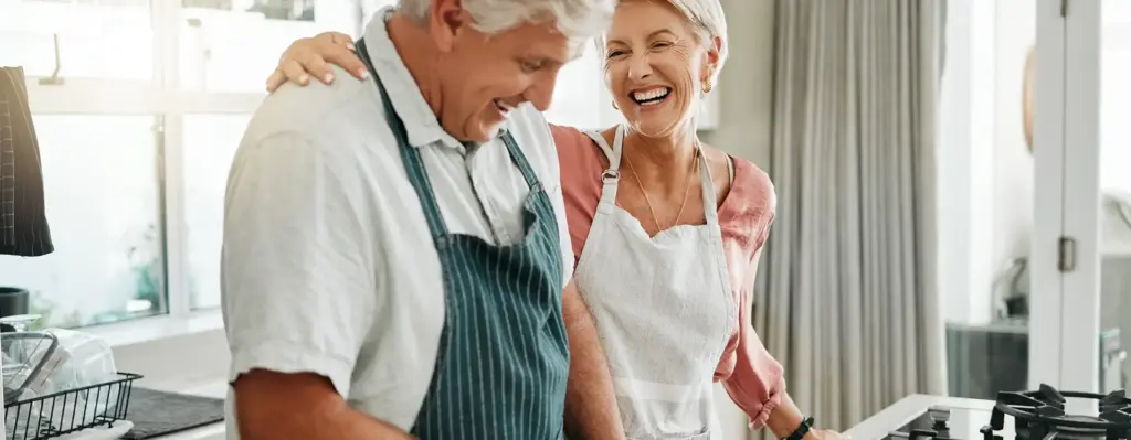 Ein älteres Pärchen steht in der Küche und kocht. Sie lachen. Das Bild wird im Bereich "Ernährungsberatung" verwendet.