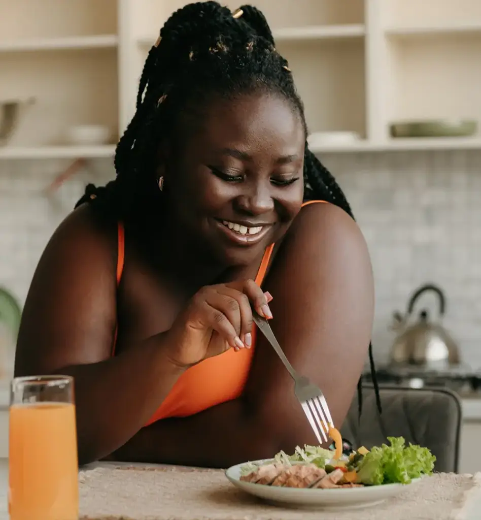 Eine Frau steht lachend in der Küche und piekt mit ihrer Gabel in einem Salat. Das Bild wird im Bereich "Ernährungsprogramm - RICHTIG ESSEN" verwendet.