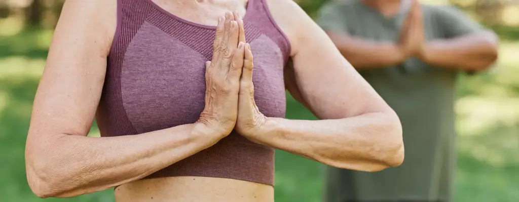 Das Bild zeigt eine ältere Person in Sportkleidung. Sie macht die Gebetshaltung, bei der die Hände vor dem Herzen zusammengelegt werden. Das Bild wird im Bereich "Fit Vital" verwendet.