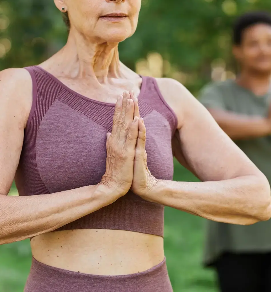 Das Bild zeigt eine ältere Person in Sportkleidung. Sie macht die Gebetshaltung, bei der die Hände vor dem Herzen zusammengelegt werden. Das Bild wird im Bereich "Fit Vital" verwendet.