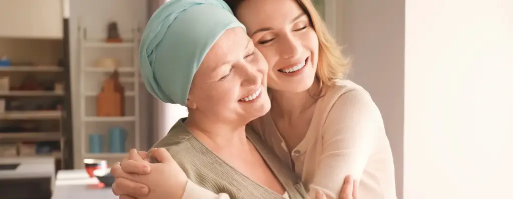 Das Bild zeigt zwei Frauen, die sich umarmen und mit ihren Wangen aneinander gelehnt stehen. Eine der Frauen hat ein Kopftuch auf. Das Bild wird im Bereich "Gendiagnostik und intensivierte Früherkennungs- und Nachsorgemaßnahmen bei familiärer Vorbelastung für Brust- und/oder Eierstockkrebs" verwendet.