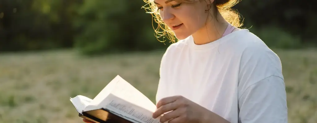 Eine junge Frau sitzt auf einer Wiese und liest ein Buch. Die Abendsonne scheint. Das Bild wird im Bereich "Gesundheitsportal VION" verwendet.