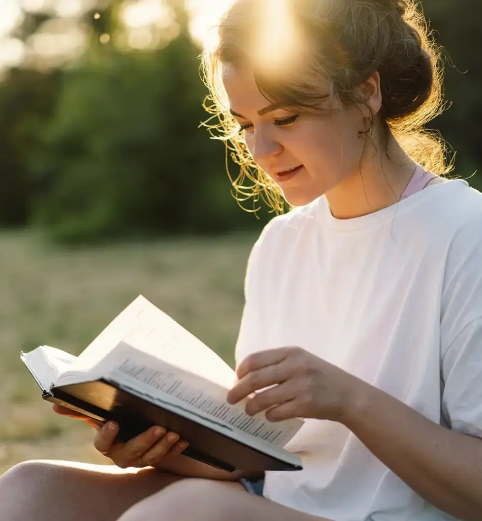 Eine junge Frau sitzt auf einer Wiese und liest ein Buch. Die Abendsonne scheint. Das Bild wird im Bereich "Gesundheitsportal VION" verwendet.