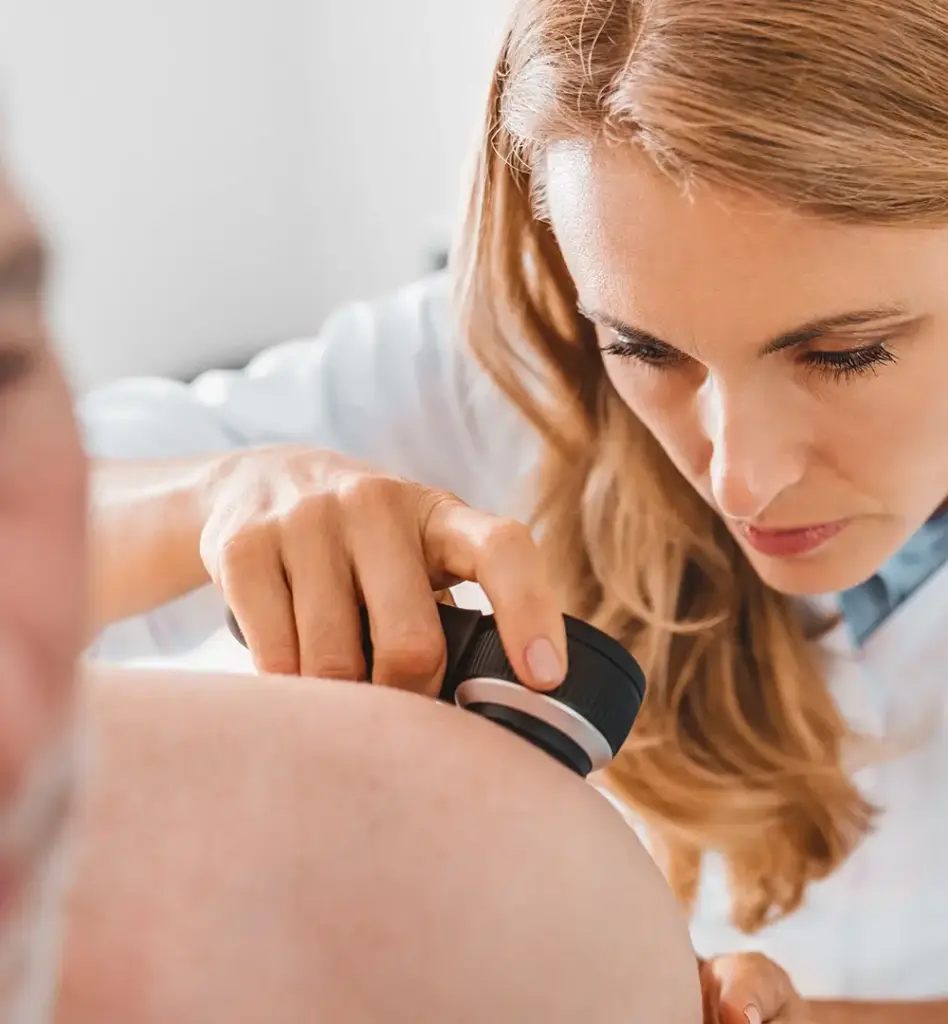 Eine Hautärztin untersucht mit einer Lupe die Haut eines Mannes. Das Bild wird im Bereich "Hautkrebs Früherkennung" verwendet.