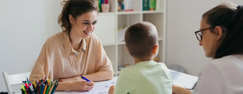 Eine Frau sitzt an einem Schreibtisch. Vor ihr sitzen ein Junge und seine Mutter. Das Bild wird im Bereich "Heilmittel" verwendet.