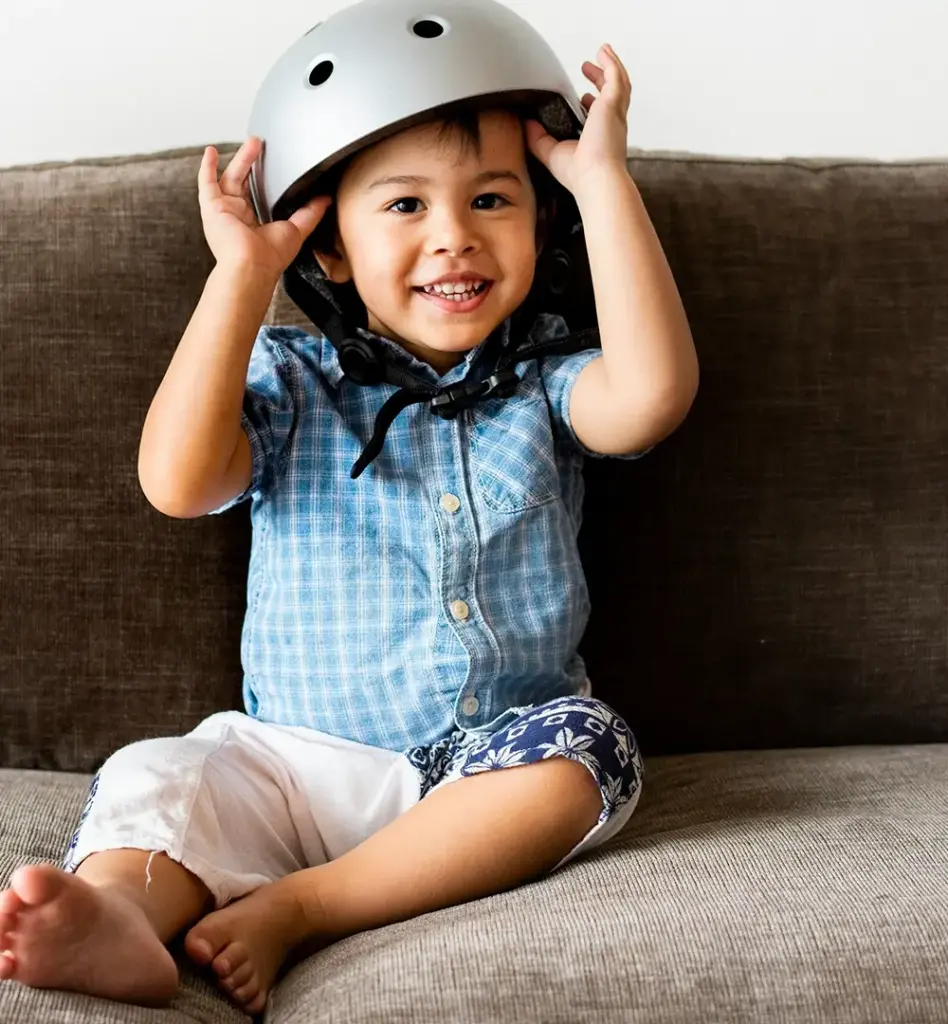 Ein kleiner Junge sitzt mit Helm auf einer Couch. Das Bild wird im Bereich "Helmtherapie" verwendet.