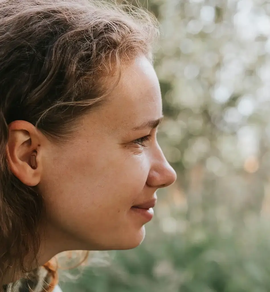 Eine Frau blickt zur Seite. In ihrem Ohr ist ein Hörgerät zu sehen. Das Bild wird im Bereich "Hilfsmittel" verwendet.