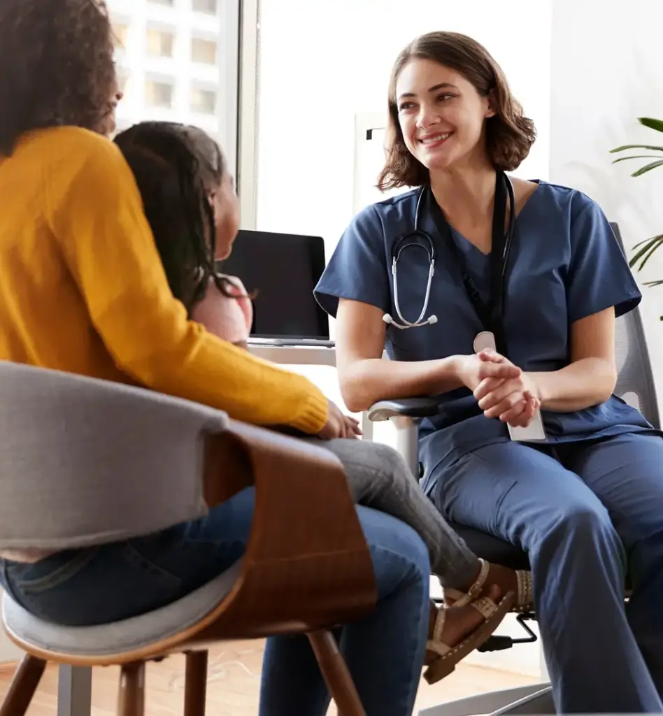 Eine Ärztin sitzt auf einem Schreibtischstuhl und ist einer Mutter mit Tochter zugewandt. Das Bild wird im Bereich "Hausarztzentrierte Versorgung" verwendet.