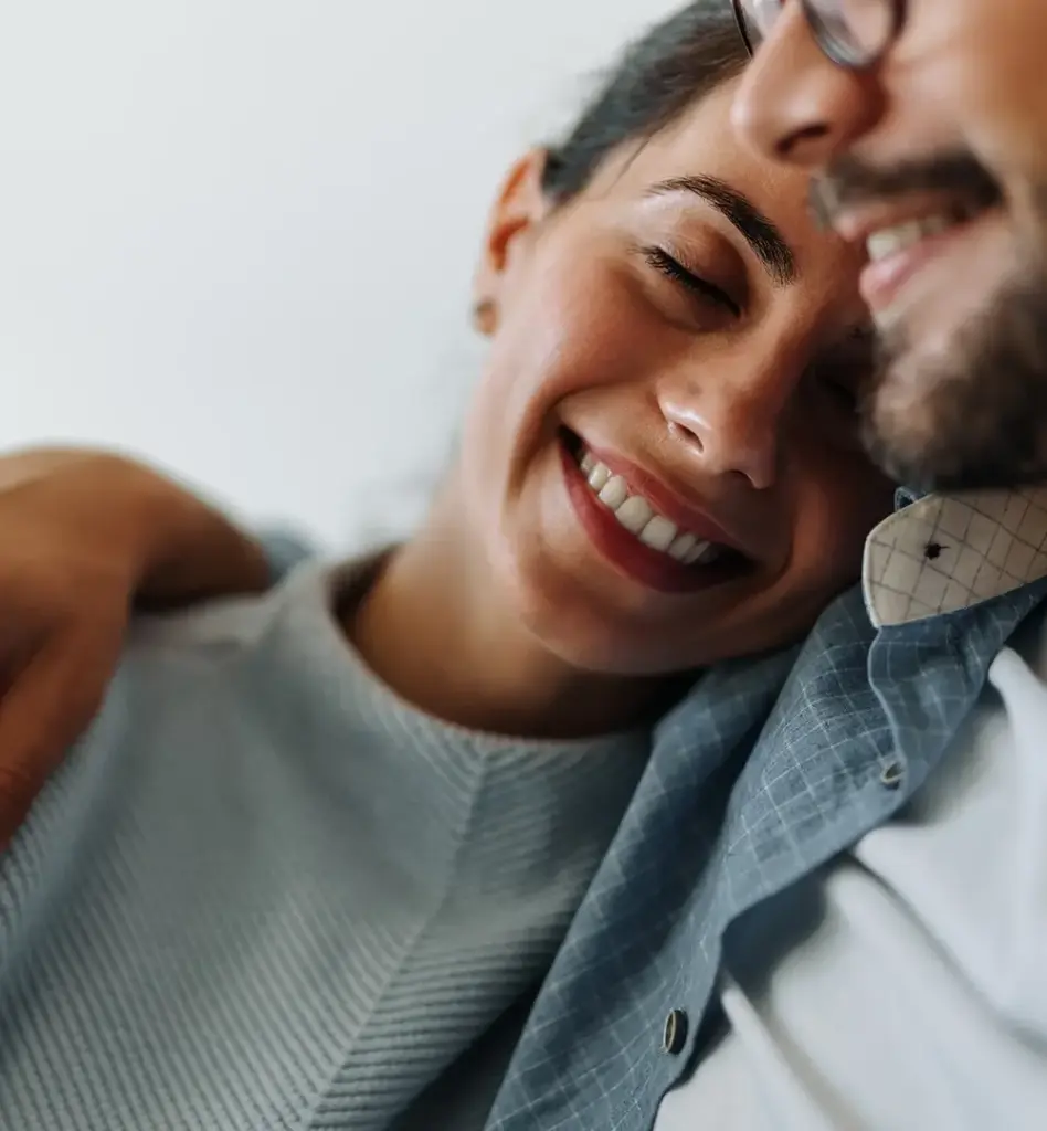 Eine Frau lehnt mit dem Kopf an der Schulter eines Mannes. Sie hat die Augen geschlossen und lächelt.