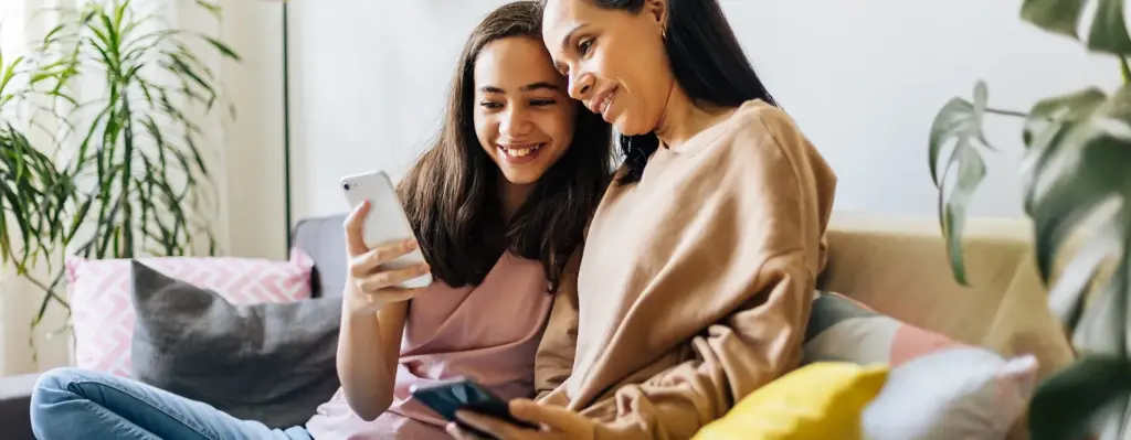 Das Bild zeigt eine Mutter und ihre Teenagertochter. Das Mädchen zeigt der Frau etwas auf ihrem Smartphone. Sie sitzen auf einem Sofa. Das Bild wird im Bereich "Mädchensprechstunde" verwendet.