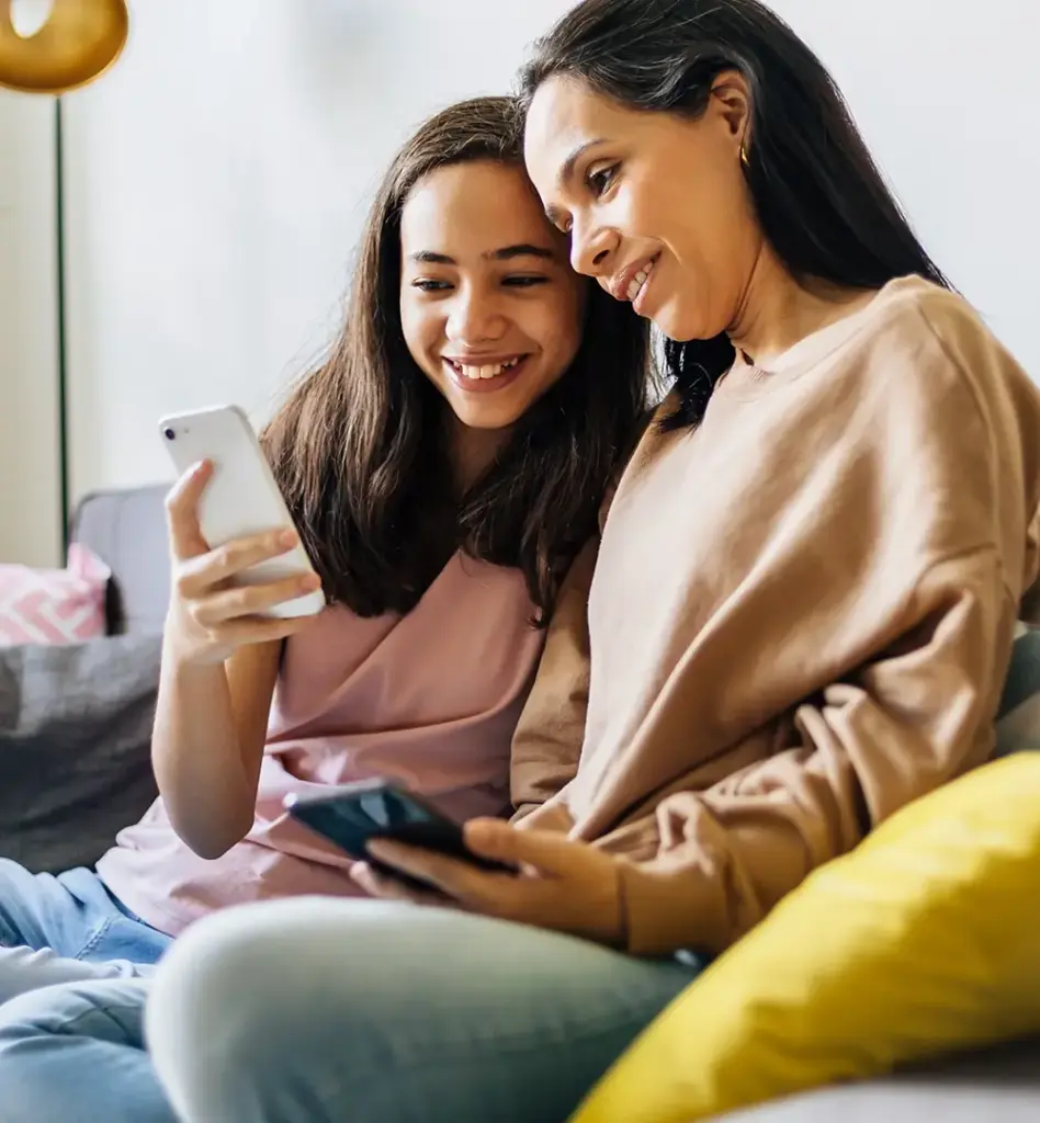 Das Bild zeigt eine Mutter und ihre Teenagertochter. Das Mädchen zeigt der Frau etwas auf ihrem Smartphone. Sie sitzen auf einem Sofa. Das Bild wird im Bereich "Mädchensprechstunde" verwendet.