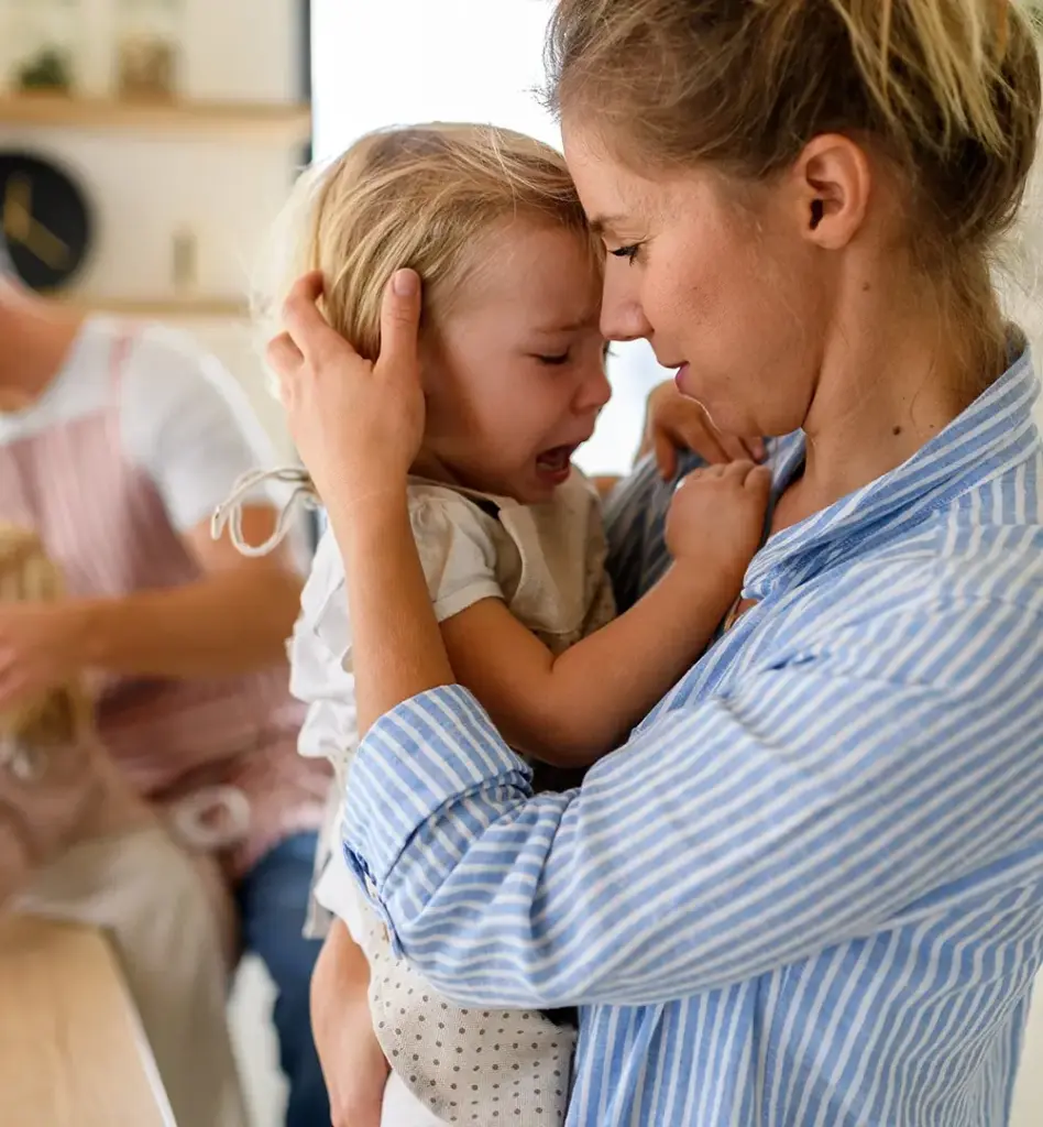 Das Bild zeigt eine Frau in Bluse, die ein kleines Mädchen auf dem Arm hat. Das Mädchen weint und die Frau tröstet es. Das Bild wird im Bereich "Mapadoo Onlinekurse für Familien" und im Blog "Kinder Grenzen setzen lernen" verwendet.