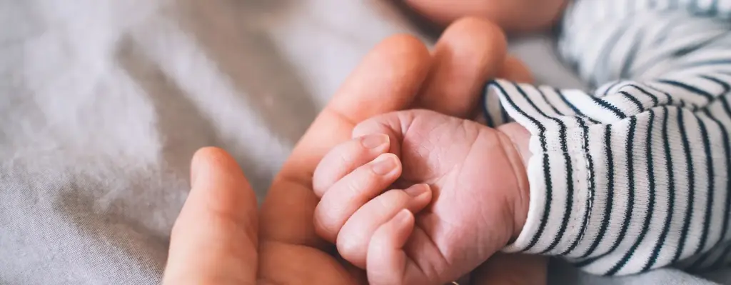 Das Bild zeigt die Hand einer erwachsenen Person. In der Hand liegt die Hand eines schlafenden Babys. Das Bild wird im Bereich "Meine pädiatrische Praxis App" verwendet.