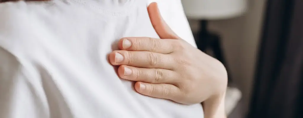 Das Bild zeigt eine Person in einem weißen T-Shirt. Die Person hält ihre Hand flach auf ihrer Brust. Das Bild wird im Bereich "Online Coach Herzgesundheit" verwendet.